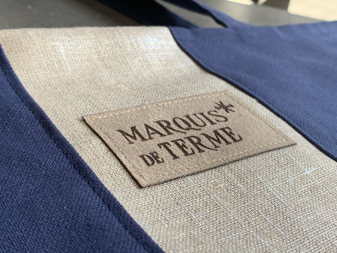 Etiquettes en suédine cuir gravé par laser produits dérivés pour le chateau marquis de terme sur des sacs conçus par Agathe and co