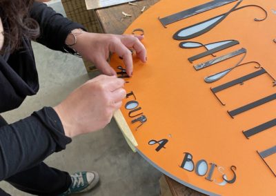 Découpe et pose de lettrage en acrylique pour un panneau signalétique en bois peint pour la boulangerie Les Pains de Nanette